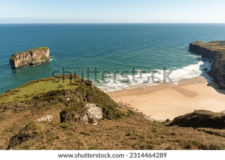 Playa deDetail shot of the golden sandy beach and calm turquoise water of the tourist village of Andrin next to impressive cliffs on the coast of Asturias on a sunny summer day