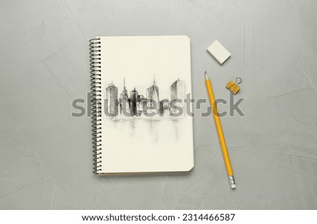 Sketch of cityscape in notebook, pencil and eraser on grey table, flat lay