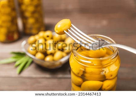 Close-up of olives on fork and glass jar on the kitchen table. pitted green olives in jar.Pickled olives in glass jar. On a wooden background.Marinaded olives. Space for text.Space for copy. 