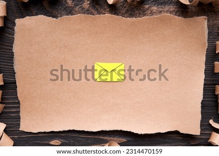 Ripped piece of paper with email icon, paper art style. Greeting card, letter, invitation mockup over dark wooden background. Flat lay, top view, copy space