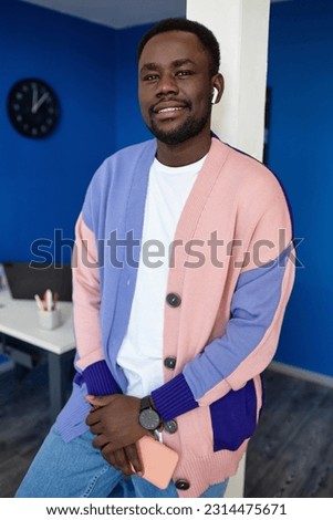 Vertical waist up portrait of modern black man wearing colorful clothes in office and smiling at camera with smartphone Royalty-Free Stock Photo #2314475671