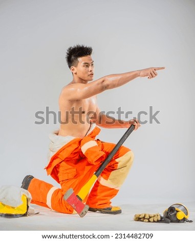 Side view shows a professional firefighter sitting and kneeling down with one hand holding an iron axe and the other hand pointing a finger. Royalty-Free Stock Photo #2314482709