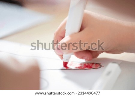 Hand of a small child drawing on a paper with a red felt-tip pen