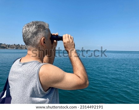 A handsome man tourist looks through binoculars at the sea