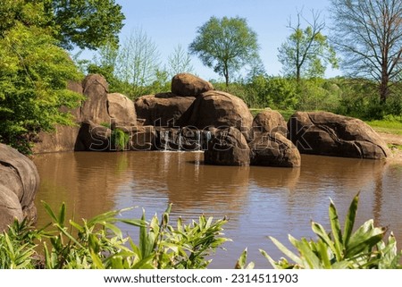 Large brown rocks and a water bond surrounded by trees located at the North Carolina Zoo in Asheboro, North Carolina