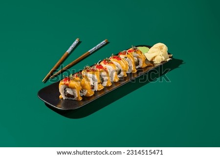 Contemporary still life of maki sushi with salmon, curry sauce, and tobiko roe on black plates against a deep green background.