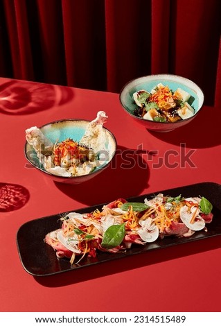 A set of Asian style snacks on a dark red velvet backdrop with hard shadows. Minimalist modern still life, diagonal composition in monochrome red. Royalty-Free Stock Photo #2314515489