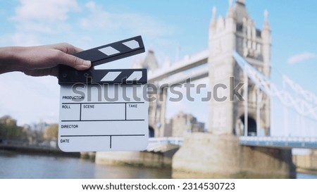 Hand is holding clapper board or movie slate with Tower Bridge background.	

