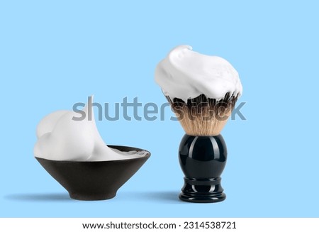 Shaving brush with raccoon fur and shaving foam in ceramic bowl on blue background. Royalty-Free Stock Photo #2314538721