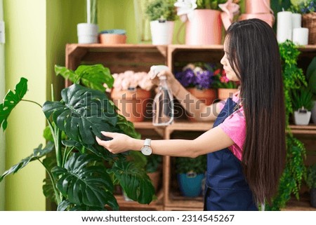 Young chinese woman florist using diffuser watering plant at flower shop