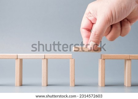 Closeup hand fill a final piece of wood between the gap of a toy bridge, solution to solve the disconnect problem Royalty-Free Stock Photo #2314572603