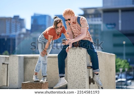Young friends hanging out, using smart phone at ledge in sunny city Royalty-Free Stock Photo #2314581193