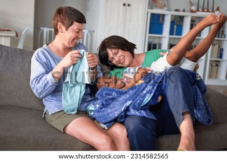 Happy lesbian couple tickling cute son on living room sofa at home Royalty-Free Stock Photo #2314582565