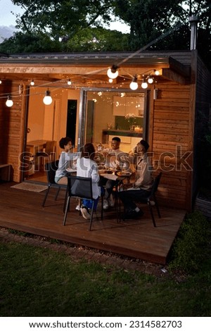 Gay couples enjoying dinner, toasting wine glasses at table on summer house patio with string lights