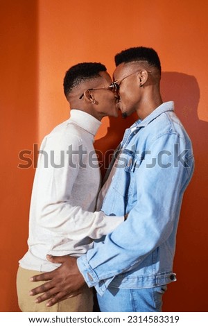 Portrait affectionate, stylish young gay male couple in sunglasses kissing on orange background Royalty-Free Stock Photo #2314583319