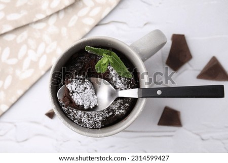 Tasty chocolate mug pie with mint and spoon on white textured table, flat lay. Microwave cake recipe Royalty-Free Stock Photo #2314599427