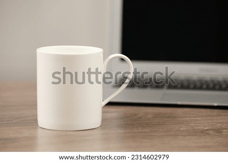 White ceramic mug and laptop on wooden table at workplace. Space for text