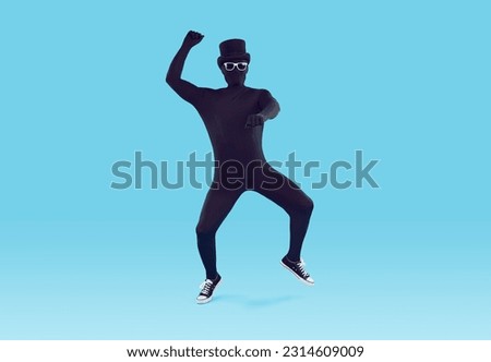 Mysterious faceless man dressed in black bodysuit dancing. Full length portrait of disguised man wearing full body spandex costume, bowler hat and sunglasses having fun over isolated studio background Royalty-Free Stock Photo #2314609009
