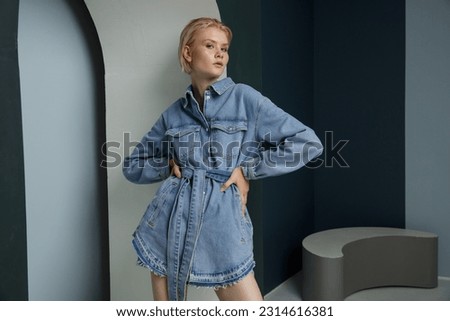 High fashion photo of a beautiful elegant young woman in pretty blue denim, jeans jumpsuit. Bicolor wall, light and dark blue. Blonde, slim figure, short haircut Royalty-Free Stock Photo #2314616381