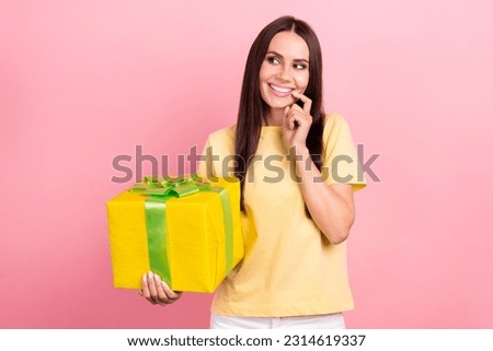 Photo of tricky cunning lady wear yellow t-shirt holding gift box finger lips looking empty space isolated pink color background