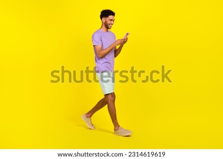 Full body cadre of guy texting his friends chatting smartphone walking streets use facebook messenger isolated on yellow color background