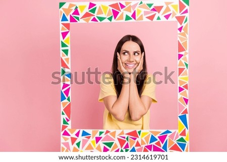 Photo of funky charming woman dressed yellow t-shirt arms cheeks empty space standing inside colorful frame isolated pink color background