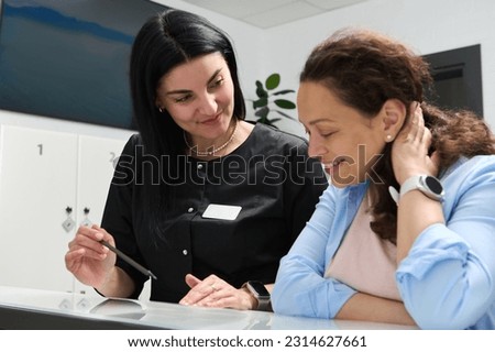 Smiling pleasant woman doctor dentist talking to a female patient, explaining the prescribed treatment, filling out forms standing at reception counter in modern dental clinic or outpatient hospital. Royalty-Free Stock Photo #2314627661