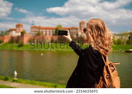 Young blonde woman tourist with stylish clothes and sunglasses making photo the famous Wawel Castle and Wawel cathedral in Krakow city. Happy vacations in Poland. High quality photo