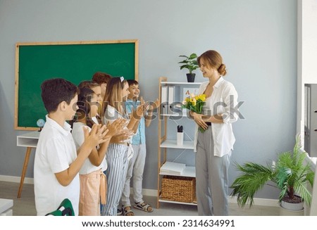 Children students giving flowers to their teacher clapping hands congratulating on holiday at elementary school. They smiling and looking at her in classroom. Good attitude, care and respect concept. Royalty-Free Stock Photo #2314634991