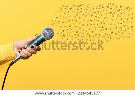 Image of a woman's hand holding a microphone on a yellow background with many musical notes floating out, suitable for use in advertising media and musical media.