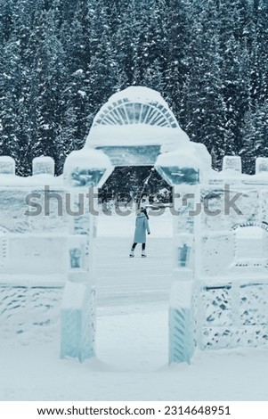 Young tourist woman with beanie in winter coat playing ice skating on frozen lake and sculpture ice wall in winter wonderland