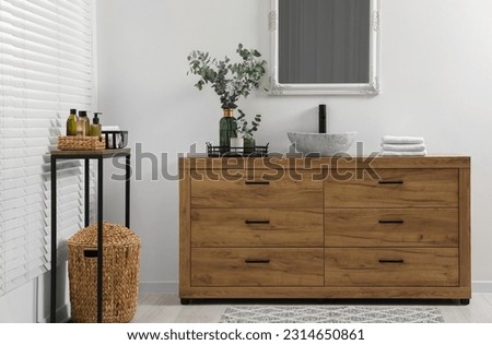 Modern bathroom interior with stylish mirror, eucalyptus branches, vessel sink and wooden vanity
