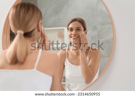 Beautiful woman removing makeup with cotton pad near mirror indoors Royalty-Free Stock Photo #2314650955