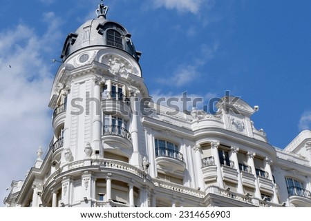 Upward view on rounded corner of classical white building in baroque architectural style with windows and balconies downtown of Madrid, Spain.