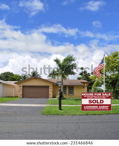 American flag pole Real Estate Sold (another success let us help you buy sell your next home) sign suburban ranch style home palm tree residential neighborhood beautiful blue sky clouds USA
