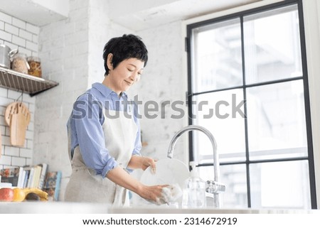 A woman is washing the dishes in the kitchen.  Royalty-Free Stock Photo #2314672919