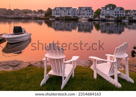 Sunrise, two white Adirondack chairs on the beach, a moored boat, and  wildfire smoke over the Mystic River marina village in Connecticut Royalty-Free Stock Photo #2314684163