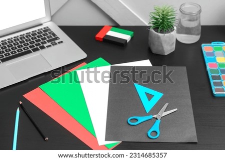 Paper sheets in colors of UAE flag with stationery on table near light wall