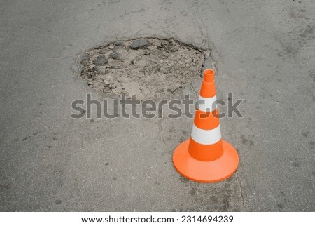 An orange cone covers a hole in the asphalt on the road.Repair of the roadway. A broken road.