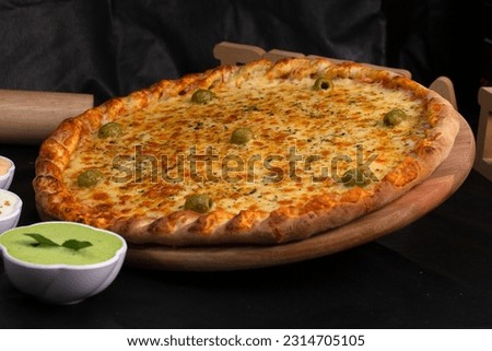 Pizza on a black background with kitchen utensils and ingredients around it, in a studio shot with a black background