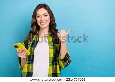 Photo of pleasant clever lovely girl dressed checkered shirt holding smartphone directing empty space isolated on blue color background