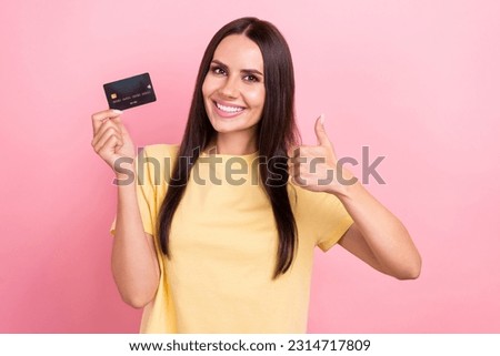 Photo of confident lucky lady wear yellow t-shirt showing thumb up rising bank card isolated pink color background