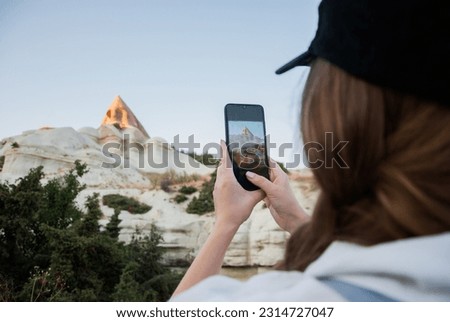 Girl taking photos of the cave temple using the phone. Close-up shot of the hand holding the phone with the mountain behind. Goreme national park of cappadocia. 
