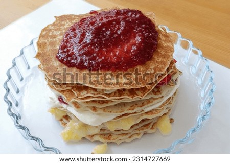 Swedish pancake cake. Several layers. Whipped cream, vanilla sauce, raspberry jam and strawberries. On a transparent plate. Royalty-Free Stock Photo #2314727669