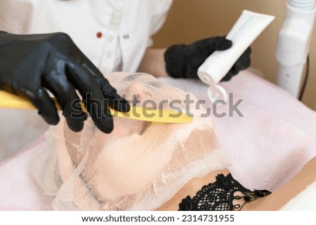 A beautician uses a spatula to apply cream to an already prepared face with gauze, a procedure for facial skin with couperosis. Royalty-Free Stock Photo #2314731955