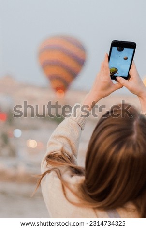 Girl taking photos of the hot air balloons using the phone. Close-up shot of the hand holding the phone with the hills and valley behind. Goreme national park of Сappadocia.