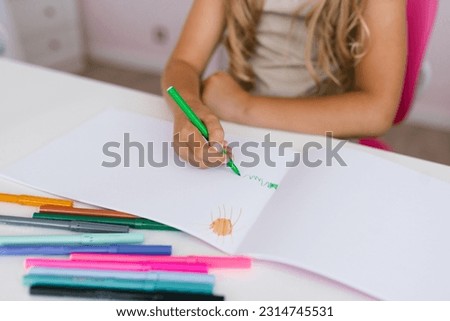 Children's hands of a schoolgirl draw the sun and grass in a notebook. Children's drawing as a hobby