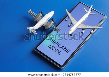 Mobile phone - smartphone with inscription "Airplane mode" on screen and toy passenger planes on blue background. Disabling communication functions of gadgets while flying in an airplane. Close-up