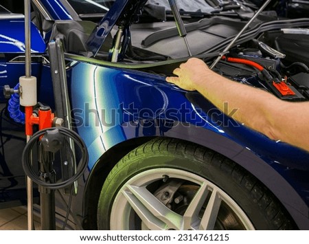 A specialist repairs a dent on the car body without painting. Process of paintless dent repair on car body. The mechanic at the auto shop with tools to repair dents in car body. Body repair. PDR.  Royalty-Free Stock Photo #2314761215