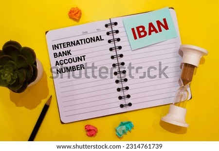 On the desktop is a white notebook with the text IBAN International Bank Account Number, a pen, burgundy and red tables, and gold-framed glasses. Business concept.